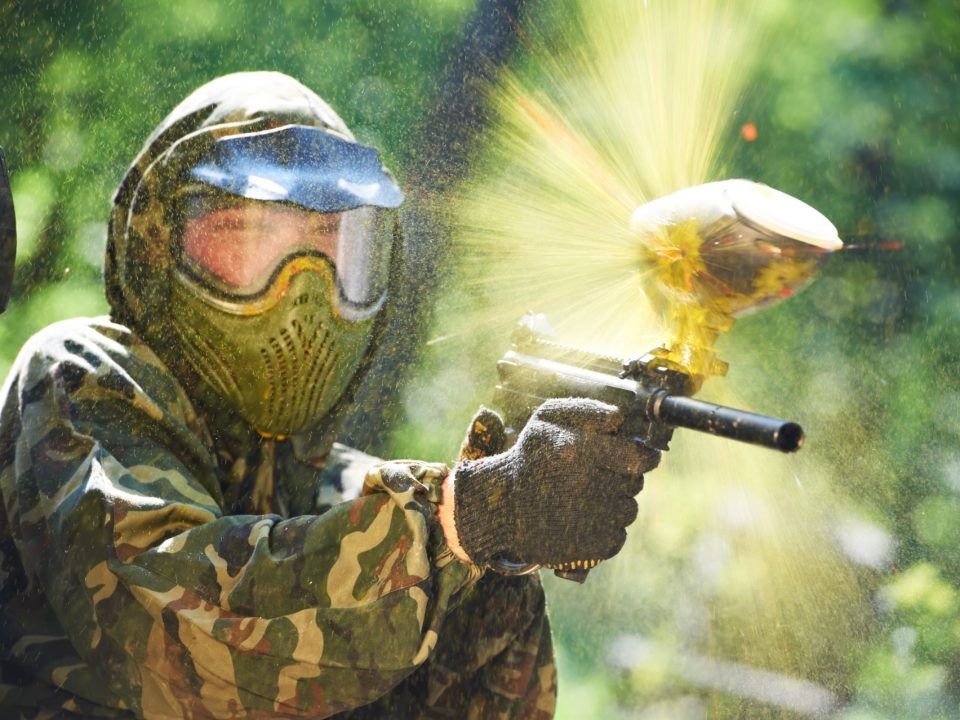 paintball sport player wearing protective mask aiming gun and shotted down with paint splash in summer